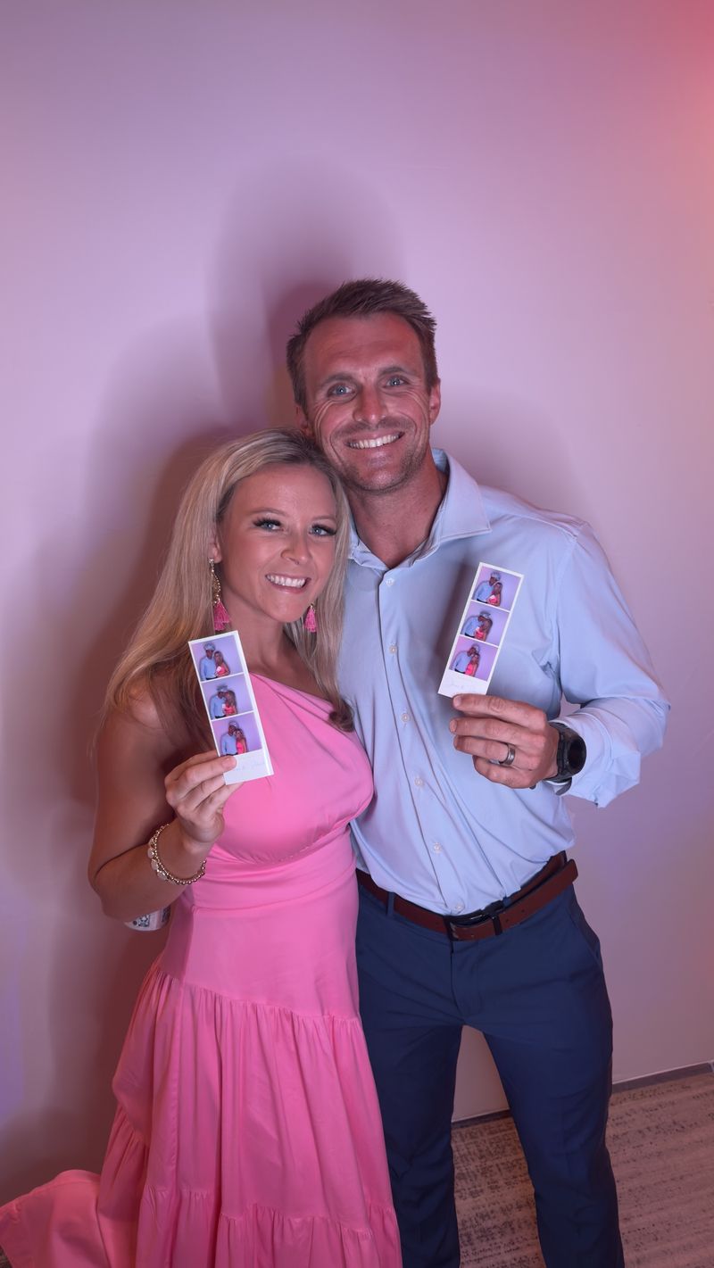 Couple holding matching photo strips under pink lighting
